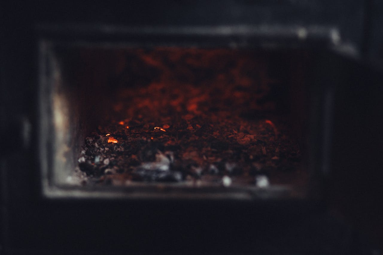 A close-up view of glowing embers and ashes in a dark fireplace, emphasizing heat and warmth.
